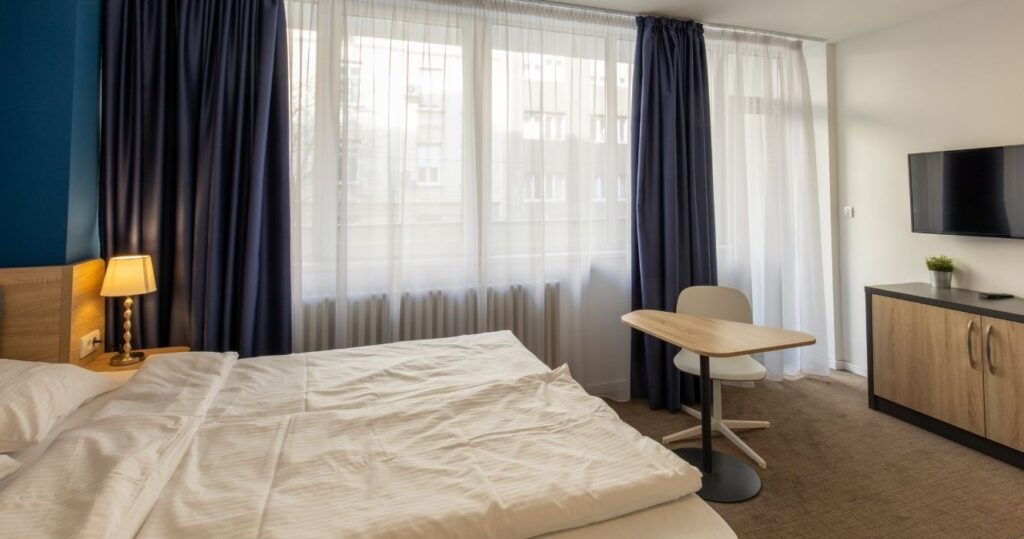 a hotel room with a desk in the center and open curtains